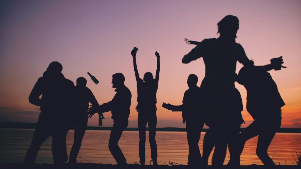 A group of friends enjoying a beach party at sunset, silhouetted against the vibrant sky.